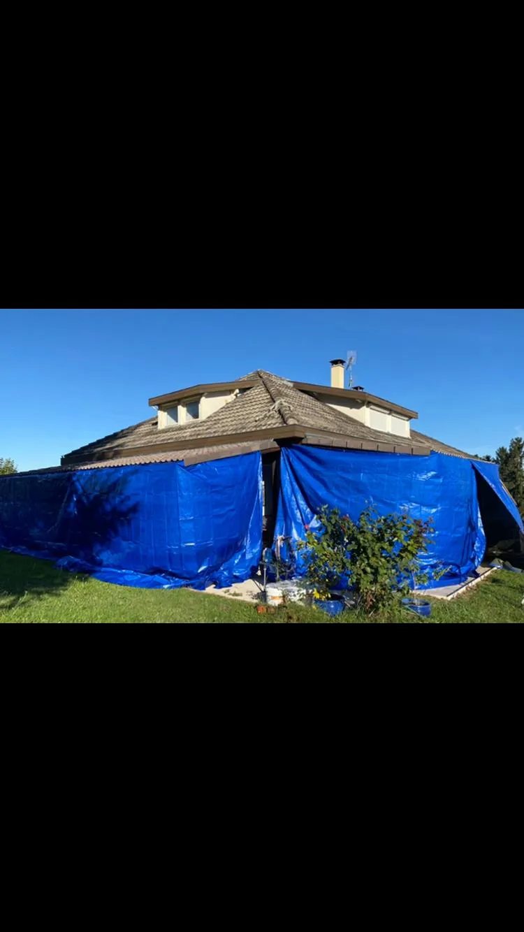 Bâchage bleu de mise hors d'eau sur les façades d'une maison pendant un chantier de toiture, dépannage après sinistre par Muller Toiture, couvreur Nord-Isère