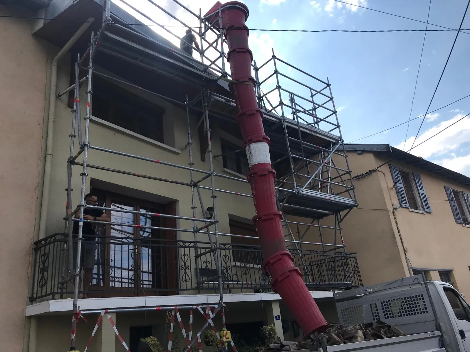 Chantier de réfection de toiture avec échafaudage de façade et goulotte d'évacuation des gravats vers une benne, par Muller Toiture, couvreur à Mions