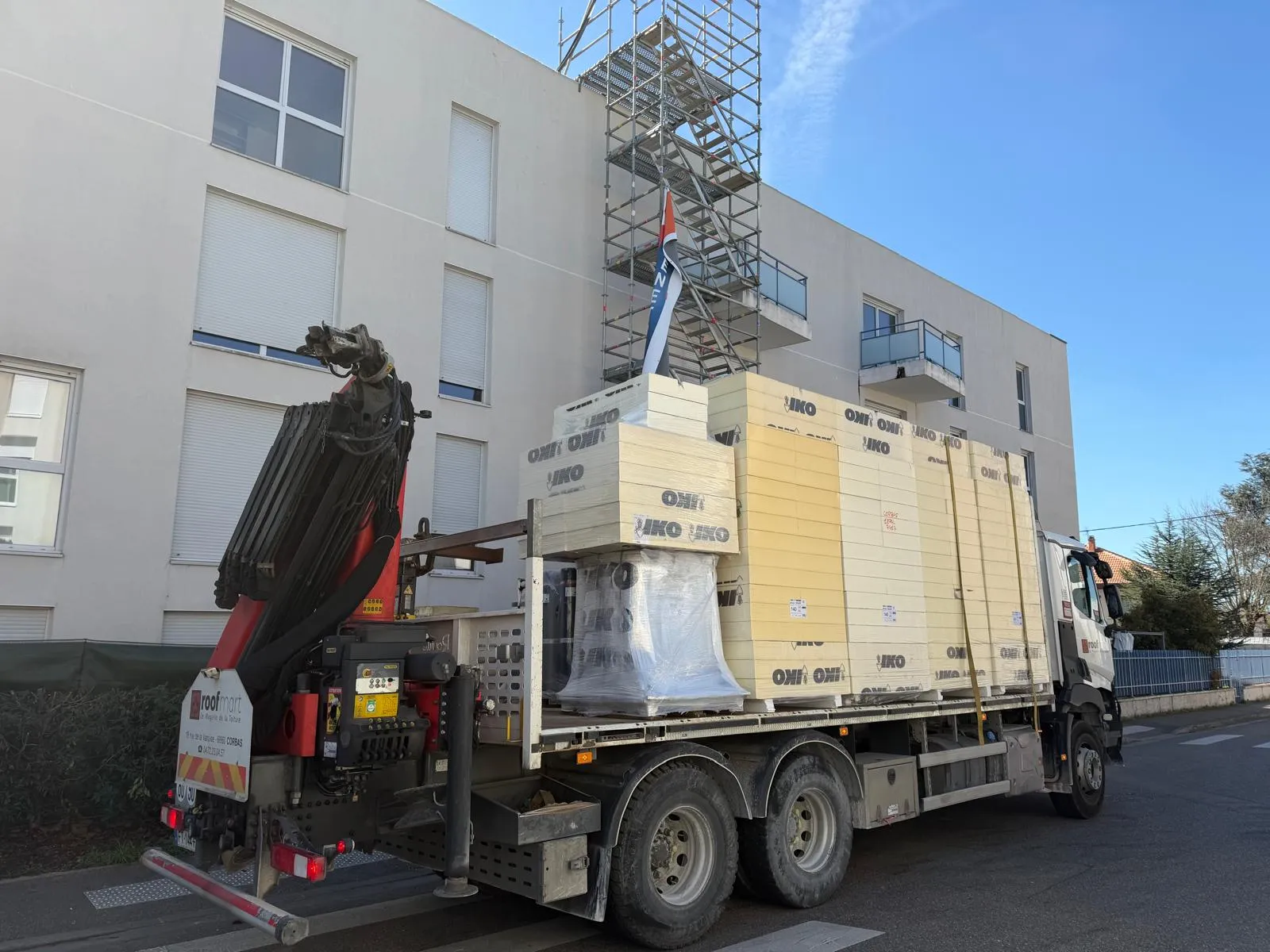 Camion-grue livrant des panneaux isolants devant un immeuble avec échafaudage, approvisionnement de chantier par Muller Toiture, couvreur dans l'Est lyonnais