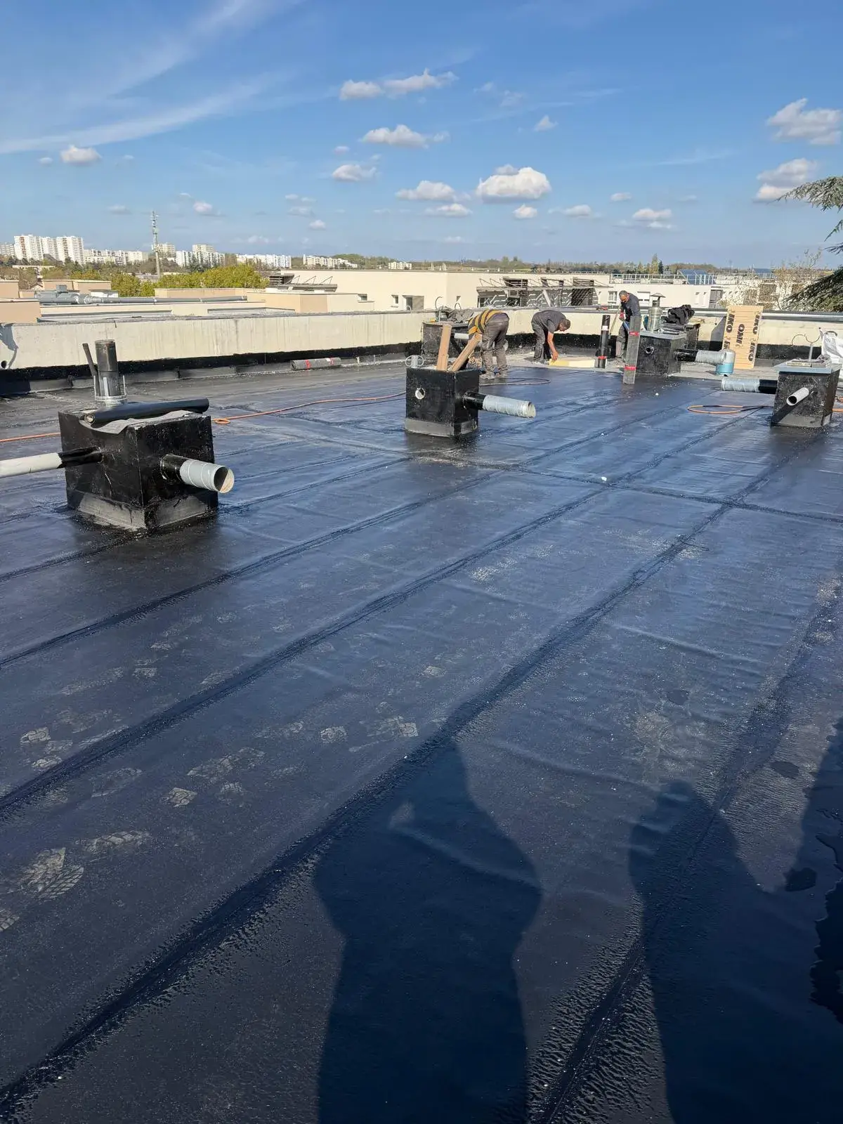 Couvreurs de Muller Toiture posant une étanchéité bitumineuse sur une grande toiture-terrasse avec évacuations d'eaux pluviales, dans l'Est lyonnais