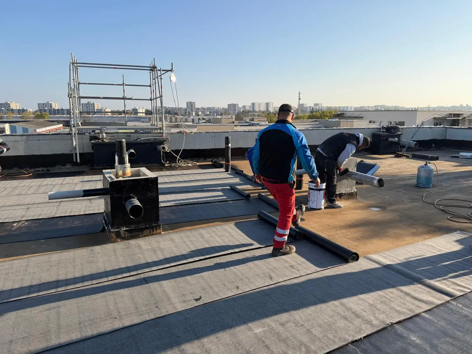 Couvreurs déroulant une membrane d'étanchéité sur une toiture-terrasse d'immeuble, réfection par Muller Toiture, couvreur dans l'Est lyonnais