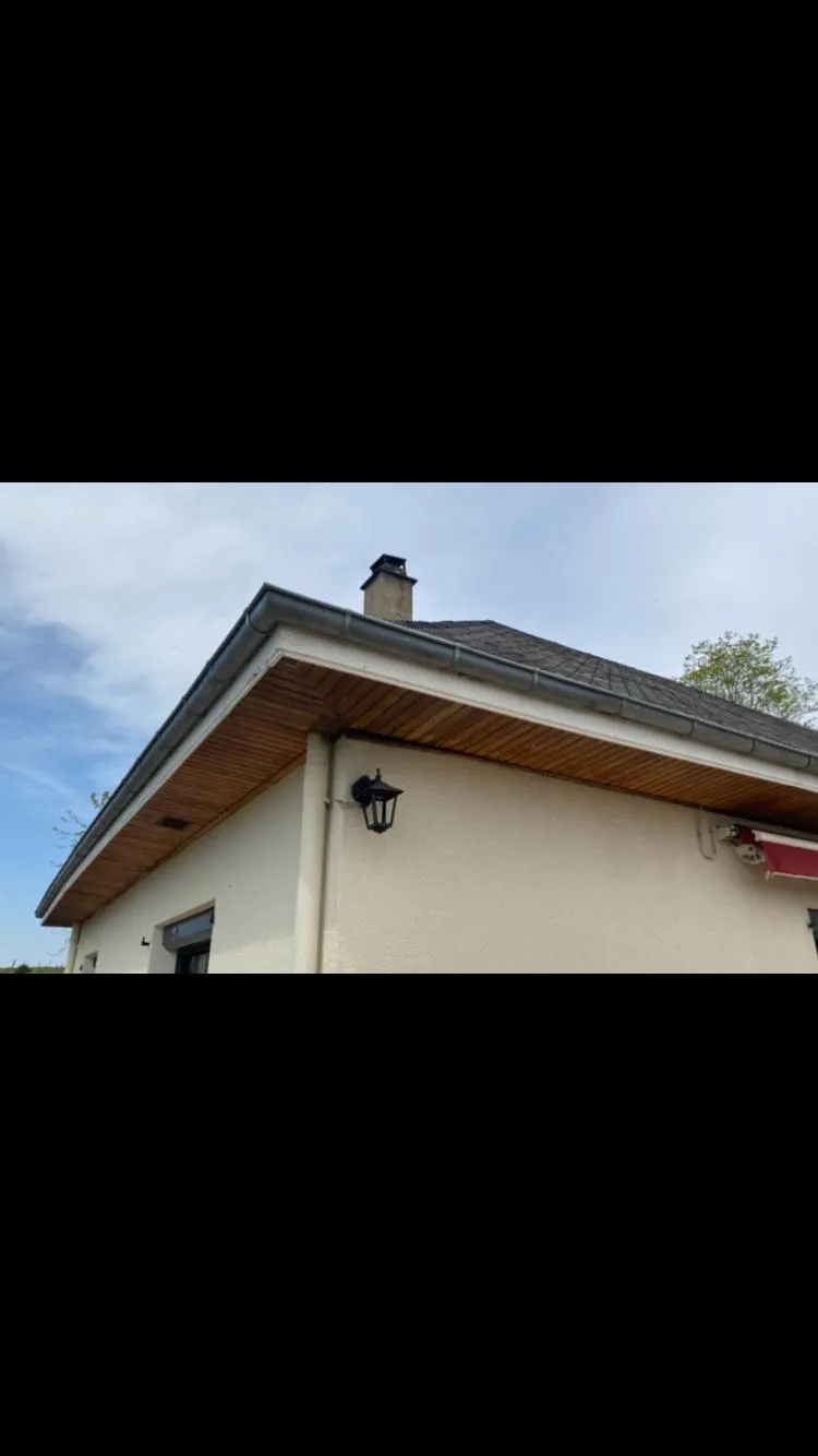 Angle de toiture terminé avec sous-face en lambris bois, gouttière en zinc et souche de cheminée, finition soignée, par Muller Toiture, couvreur dans l'Ain